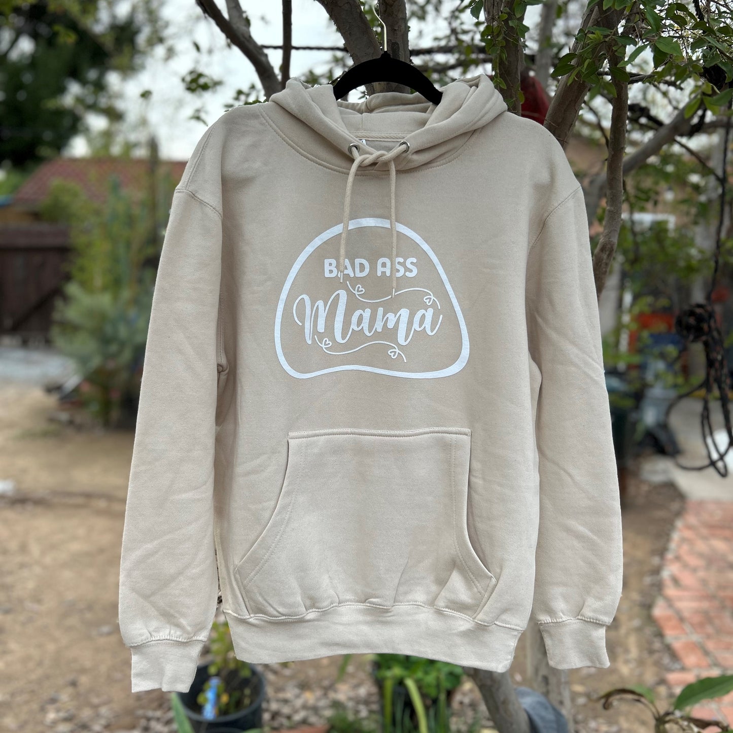Release your Bad Ass Mama side with our cream hoodie, featuring a bold design that's perfect for fierce women. For the fearless and confident women who aren't afraid to show off their attitude, the Bad Ass Mama Cream Hoodie is a must-have wardrobe essential. The high-quality direct-to-garment design showcases bold font letters spelling out "Bad Ass Mama" against a cream-colored background that will make you stand out from the crowd.