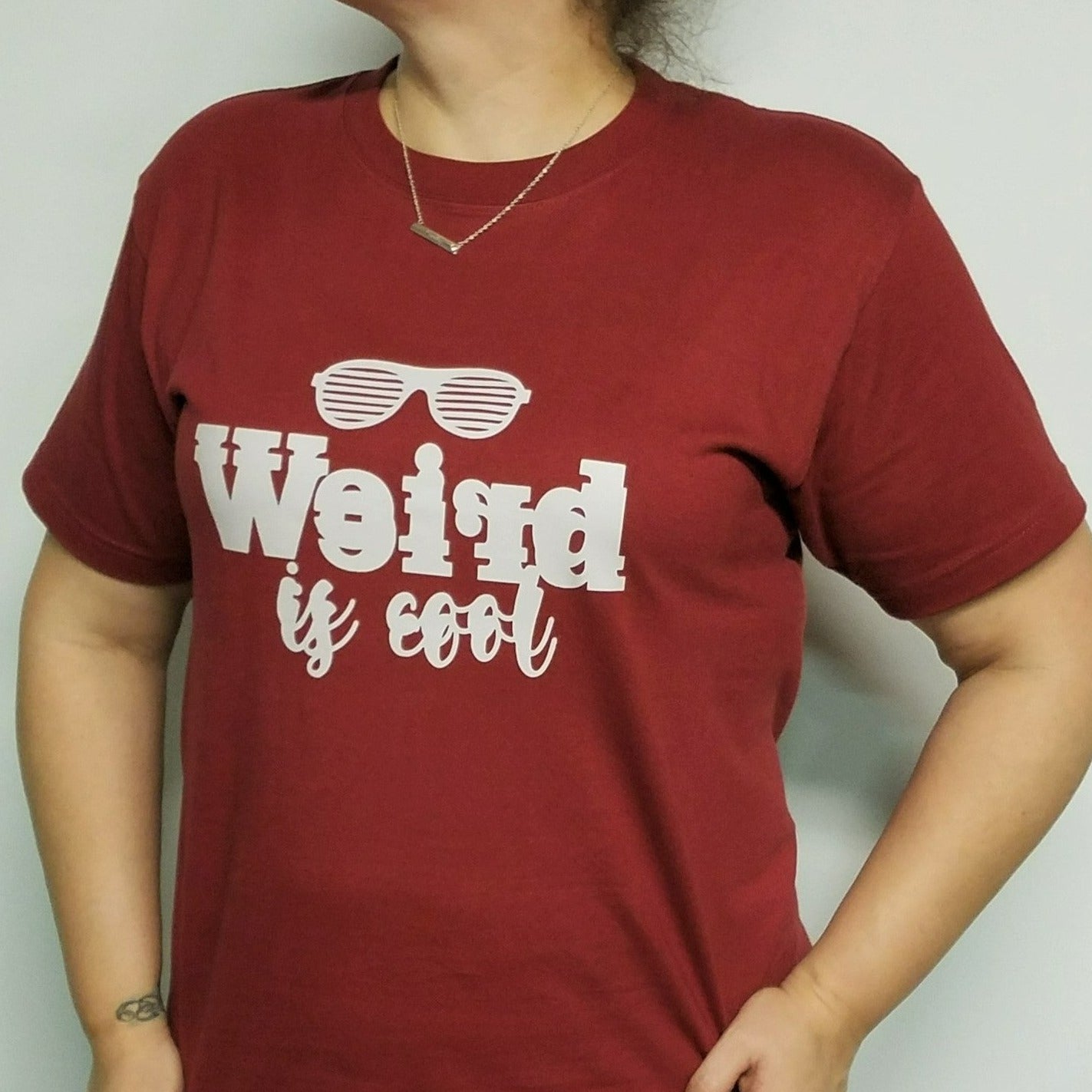 Our "Weird is Cool" women's t-shirt is professionally screen printed featuring a wine-colored shirt with blurred light gray letters and a pair of sunglasses over top. I'll be honest, I love all things weird. Quite frankly, I can be a big weirdo myself sometimes. But when the daughter of a good friend was being called "weird" at school, it bothered me because being weird is what makes us special and different - and it's okay to be different, even cool!